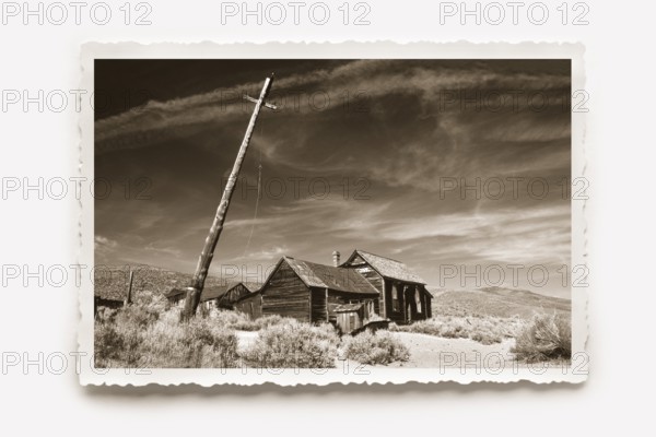 Lonely wooden house in Bodie, in front of it a crooked lamp post. Dry grass and undergrowth in the