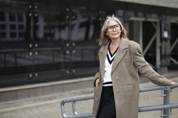 An older woman with gray hair and glasses exudes confidence while leaning against a railing in