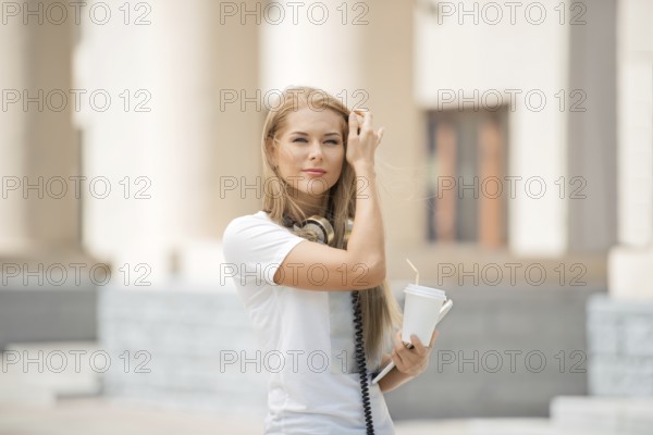 Cheerful young woman with vintage headphones around her neck, holding a coffee cup with a straw and
