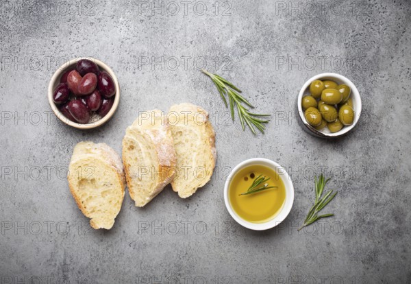Slices of fresh ciabatta, green and brown olives, olive oil with rosemary, olive tree branches on