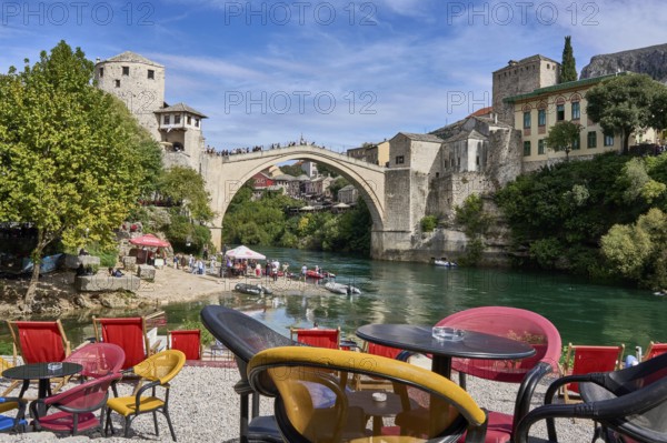 Cafe with colourful chairs on the bank of the river Neretva, behind the bridge Stari Most, numerous