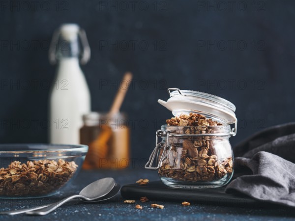 Homemade granola in glass jar on dark table. Ingredients for healthy breakfast - granola, milk and