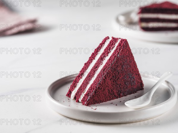 Piece of red velvet cake with perfect texture in matte plate on white marble tabletop. Slice of