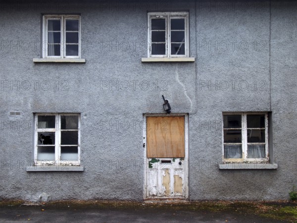 An old abandoned grey derelict house on a residential street with dirty broken windows and a