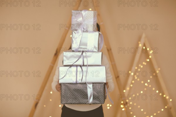 Female holding big stack of presents wrapped in brown paper with white bows on simple background