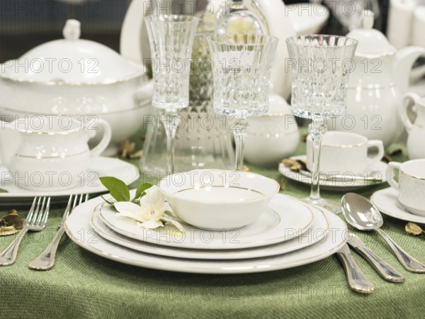 Set of new dishes on table with green tablecloth. Stack of white plates with flowers on restaurant
