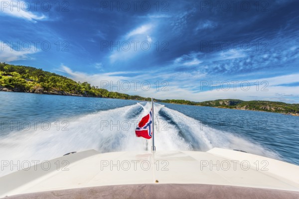 Speed boat swiftly crossing a sunny fjord in southern Norway sporting the Norwegian flag.