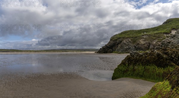 View of the picturesque golden sand Maghera Beach with algae-covered rocks and cliffs in the