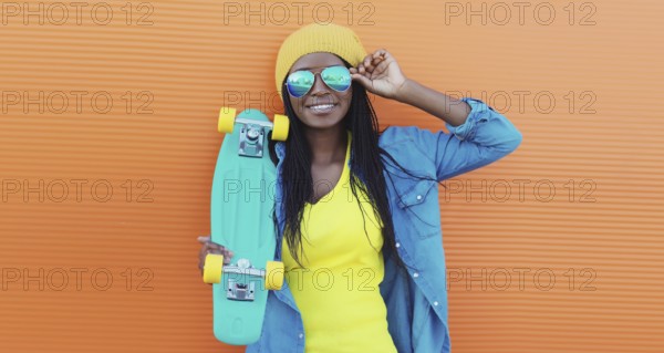 Summer portrait of stylish happy African young woman with skateboard, modern black teenage girl in