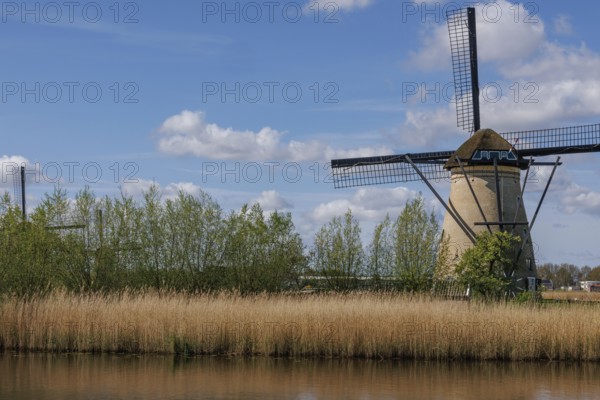 A traditional windmill in a wide landscape with meadow, water and cloudy sky on a summer's day,