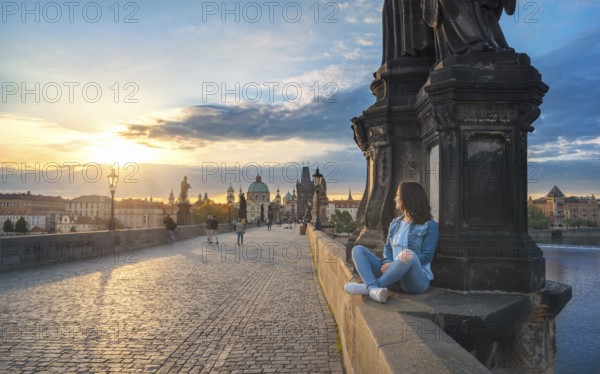 Young brunette woman, sitting relaxed on the Charles Bridge walls, over the Vltava river, admiring