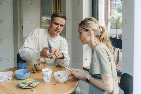 Ein Ehemann zeigt seiner Frau die Nachrichten auf seinem Handy, während er beim Frühstück am Tisch
