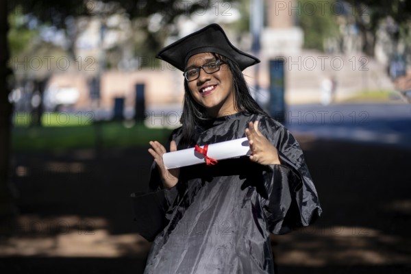 Latin transgender woman recent graduated, dressed in cap and gown, showing off his degree