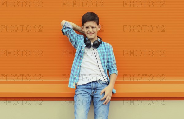 Portrait of happy modern teenage boy listening to music with headphones in the city on orange wall