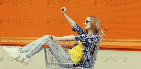Stylish happy young woman taking selfie with phone, cool modern teenage girl having fun sitting in