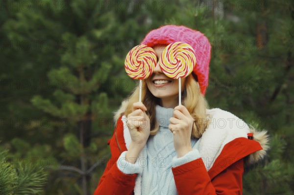 Winter portrait of happy funny smiling young woman having fun with sweet lollipop wearing hat