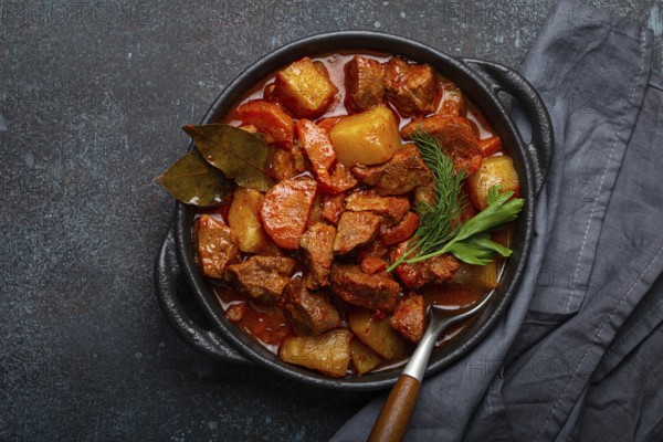 Beef meat stew with potatoes, carrot and delicious gravy in black casserole pot with bay leaves and