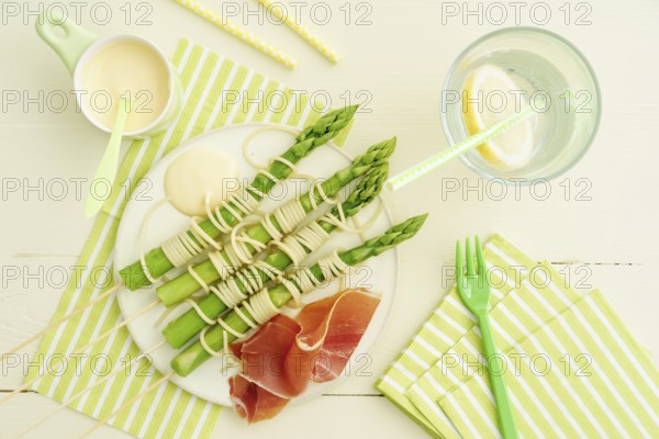 Steamed green asparagus on wooden skewers with spaghetti wrapped in hollandaise sauce and ham