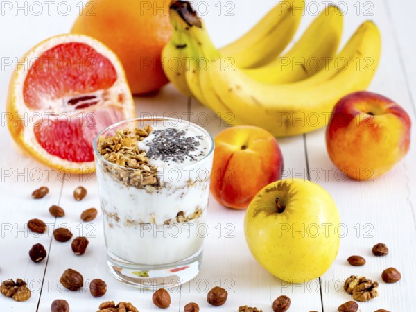 Healthy breakfast: yogurt with muesli and chia seeds, fruits and nuts on white wooden background.