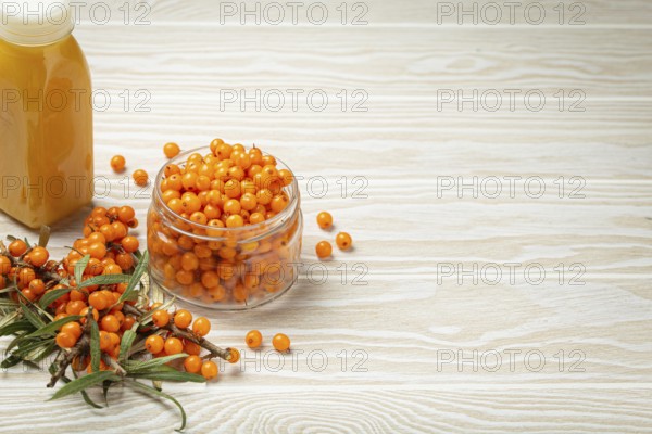 Sea buckthorn healthy drink in bottle, ripe berries in glass jar and branches with leaves top view