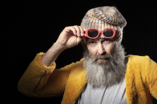 An elderly man with a grey beard wearing a knitted hat and a bright yellow fur coat. Fashionable