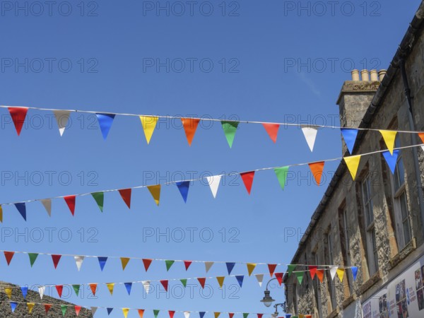 Colourful flags hang over a street corner between historic buildings under a cloudless blue sky,