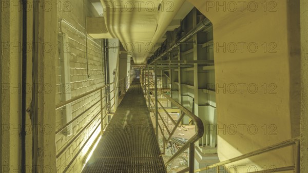 Industrial interior with a raised walkway and metal grating, surrounded by pipes and railings, Bad