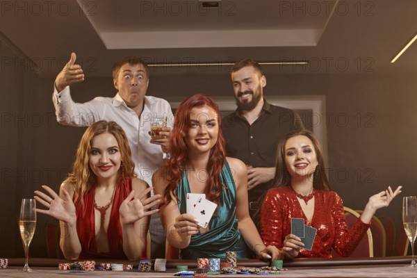 Happy friends are playing poker at casino. They are celebrating their win, smiling and posing at