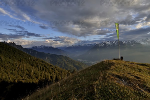 Sitting woman enjoying a dreamlike evening mood in the mountains, view to the Rätikon, flag of the