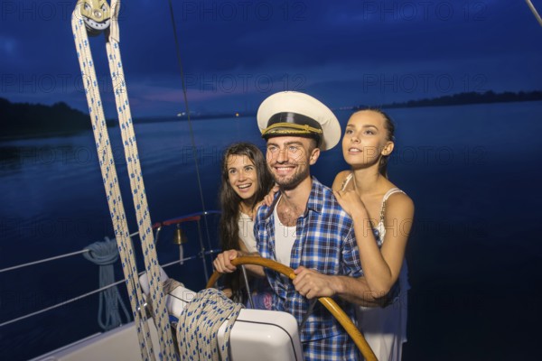 Captain with girls on the yacht. Night cruise on the yacht. Friends traveling by yacht on the river