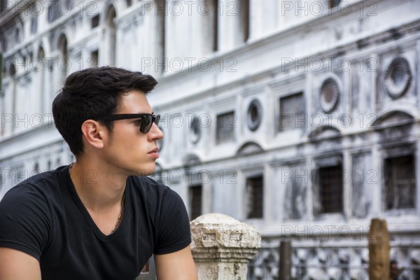 Portrait of Attractive Dark Haired Young Man Leaning Against Railing on Foot Bridge Over Narrow
