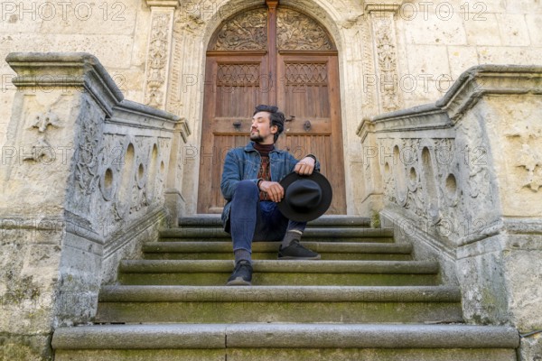 Portrait of a young man sitting against a beautiful old medieval cathedral door. A man in front of