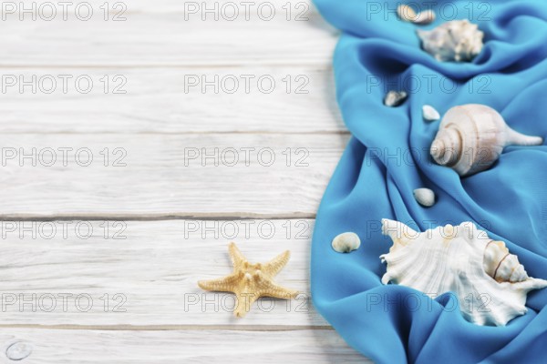 Seashells, blue fabric and starfish on white planks vacation planning background flat lay with