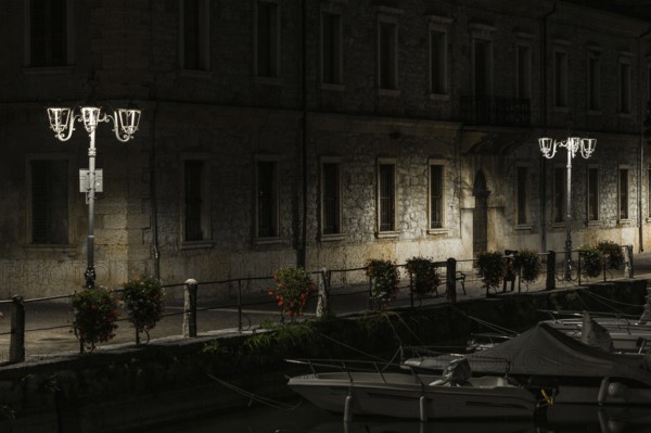 A canal view at night with moored boats, a stone building, and lampposts creating tranquil shadows,