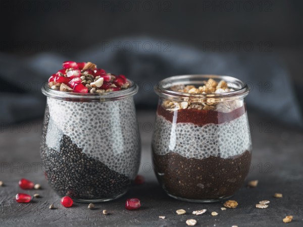 Two chia pudding in glass jars on dark table. Two colors charcoal chia puding with pomegranate,