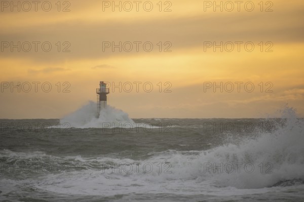 A lighthouse stands in the storm. Wild sea in the evening. Sunset on a coast with many rocks in the