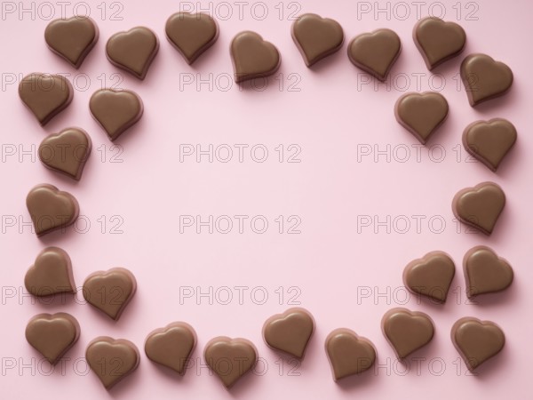 Frame of romantic chocolate confections in heart shapes on pastel pink background. Canvas with