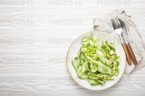 Healthy vegan green avocado salad bowl with sliced cucumbers, edamame beans, olive oil and herbs on