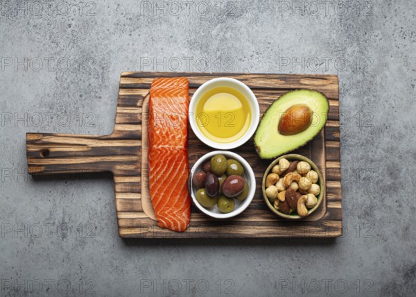 Food sources of healthy unsaturated fat: fresh raw salmon fillet, avocado, olives, nuts on cutting