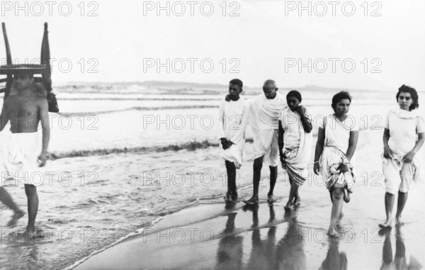 Mahatma Gandhi and others walking Juhu Beach, Mumbai, May 1944, Kanu Gandhi, carrying a chair on