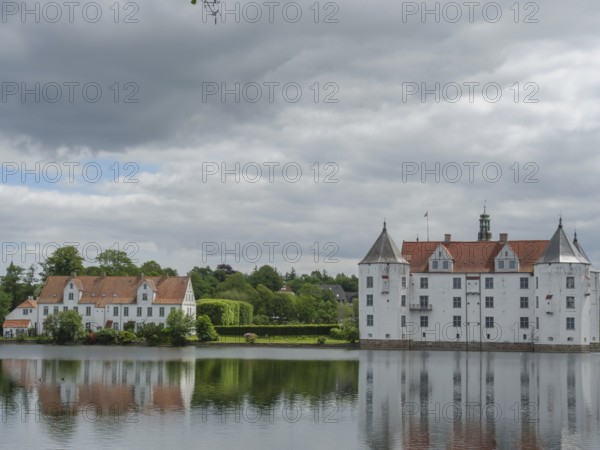 A historic castle with white facades and red roofs is reflected in a calm body of water under a