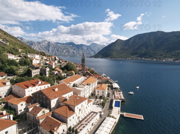 Old houses with red roofs on the shore of the Bay of Kotor with a swimming pool on the promenade.