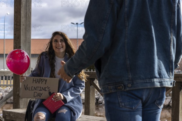 Young woman with a happy valentine's day sign, a balloon of hearts and a red gift, giving a