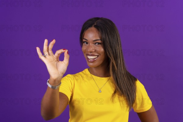 Studio portrait with purple background of an african smiling urban woman gesturing agreement with