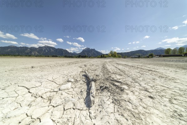 Cracked, dried out ground, waterless Forggensee in spring, behind it Tegelberg massif and Säuling,