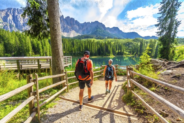 Tourists walking on a path towards the turquoise waters of lake carezza, surrounded by the stunning