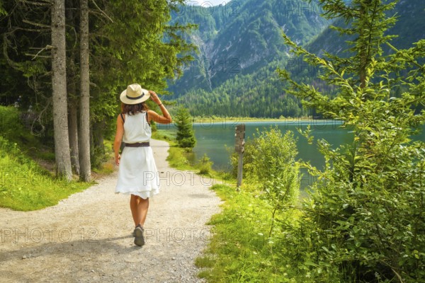 Tourist walking on a path near lake dobbiaco, enjoying the summer landscape in the dolomites