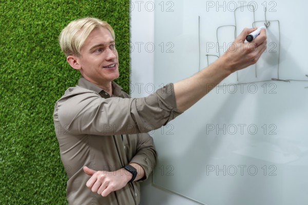 Young businessman drawing growing bar chart on whiteboard during a presentation in a modern office