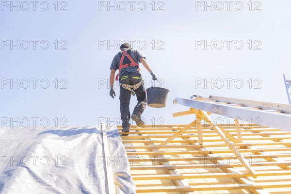 A worker in safety clothing climbs a ladder to work on a roof, in sunny weather, roof renovation,
