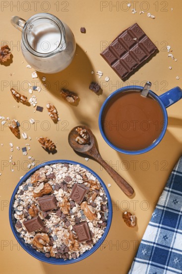 Breakfast, muesli with chocolate and walnuts next to milk and coffee from above on a yellow